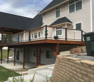Corner view from the ground of a newly built wooden deck with metal and wire railings installed by Tip Top Construction.
